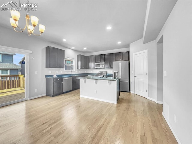 kitchen featuring dark countertops, a kitchen island, appliances with stainless steel finishes, a kitchen breakfast bar, and decorative light fixtures