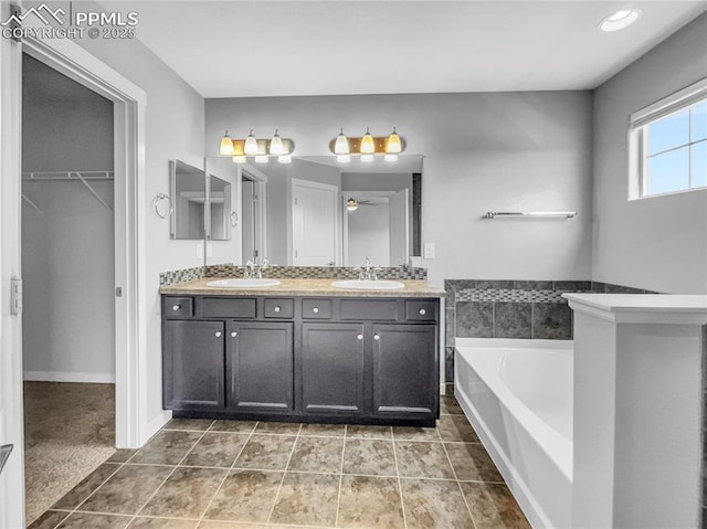 bathroom featuring a garden tub, double vanity, a sink, and a walk in closet