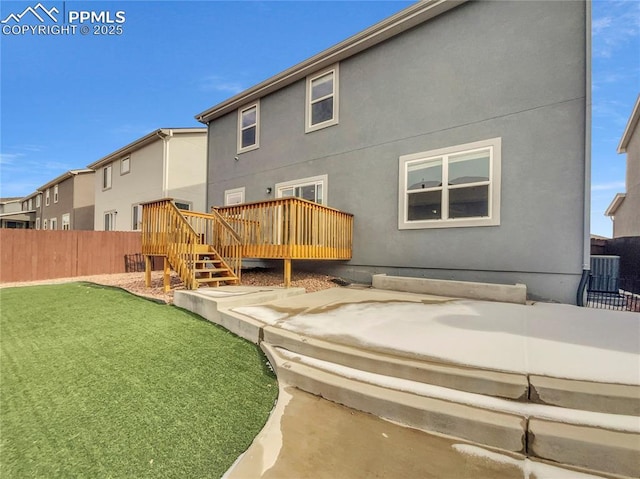 back of property featuring a deck, central air condition unit, fence, a yard, and stucco siding