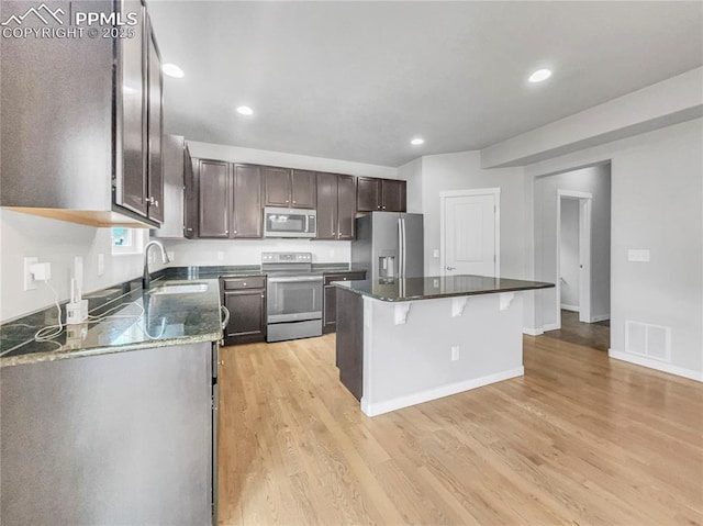 kitchen with visible vents, appliances with stainless steel finishes, a kitchen island, a sink, and a kitchen bar