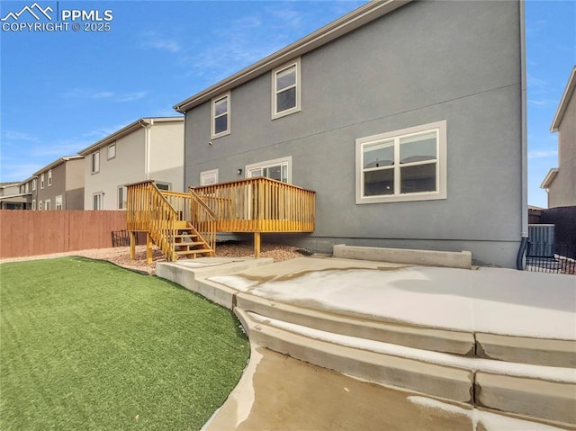 rear view of house with a lawn, fence, a wooden deck, central AC, and stucco siding