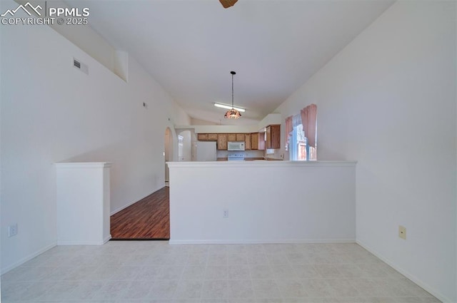 kitchen featuring brown cabinets, visible vents, vaulted ceiling, white appliances, and a peninsula