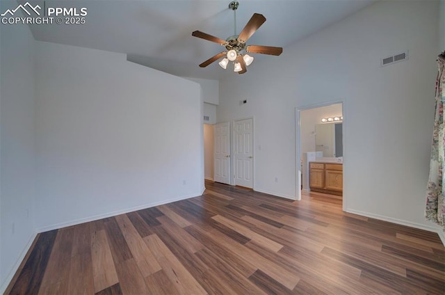 unfurnished bedroom with baseboards, visible vents, ensuite bath, wood finished floors, and high vaulted ceiling