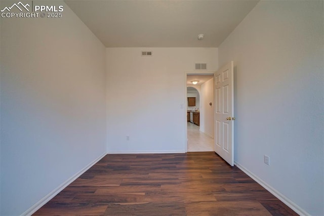 empty room with arched walkways, visible vents, and wood finished floors