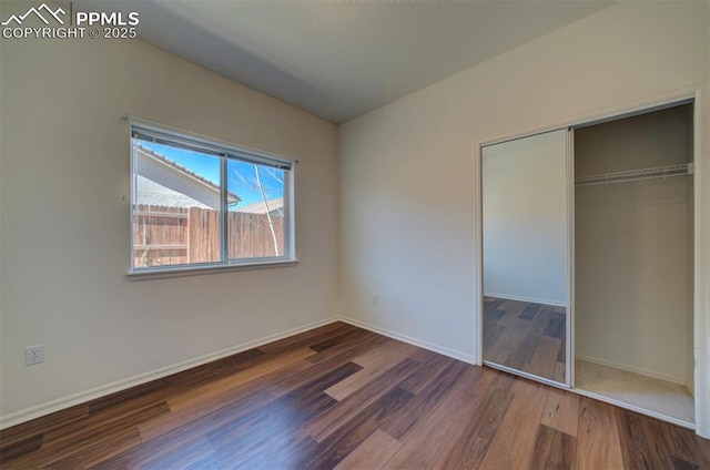 unfurnished bedroom with lofted ceiling, a closet, wood finished floors, and baseboards