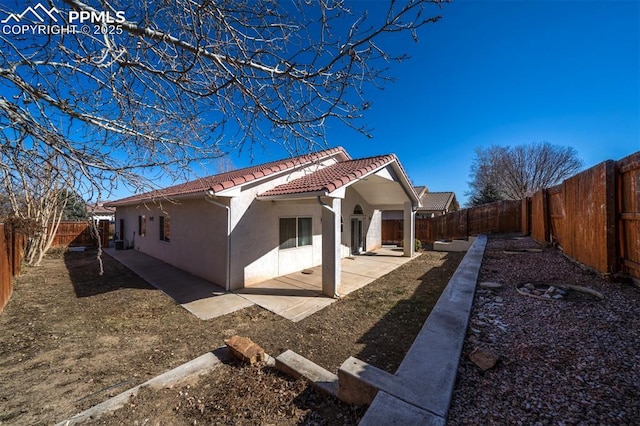 view of side of property featuring stucco siding, a tile roof, a fenced backyard, and a patio