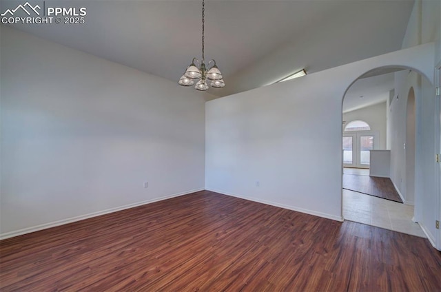 empty room with baseboards, arched walkways, lofted ceiling, wood finished floors, and an inviting chandelier