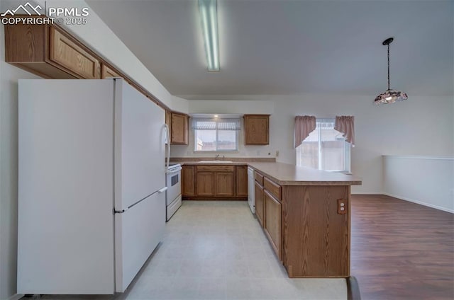 kitchen with a peninsula, white appliances, light countertops, brown cabinetry, and pendant lighting