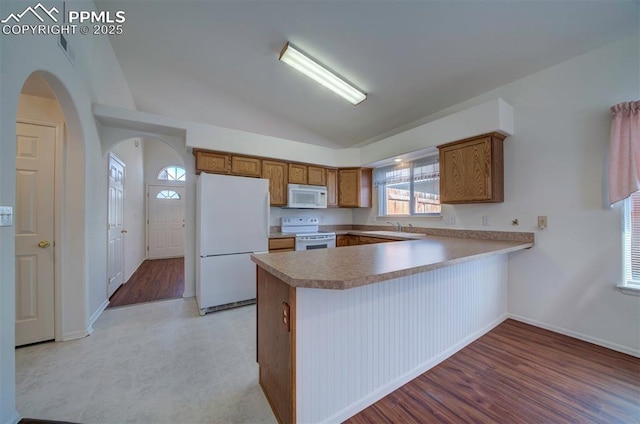 kitchen with arched walkways, a peninsula, white appliances, vaulted ceiling, and brown cabinets