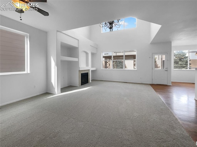 unfurnished living room with a tile fireplace, built in shelves, ceiling fan, and wood-type flooring