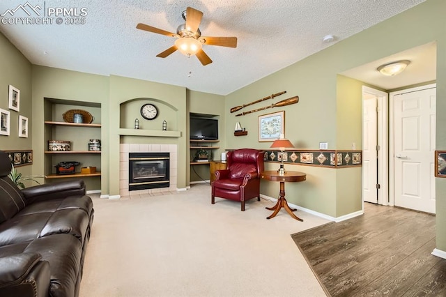 living room with a textured ceiling, built in shelves, a tile fireplace, and baseboards