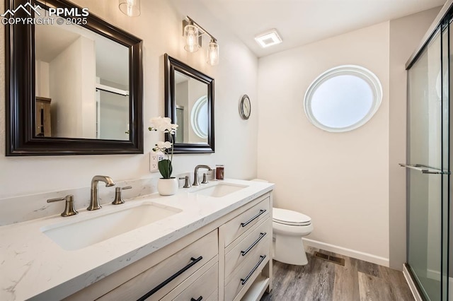 full bath featuring a shower with shower door, visible vents, a sink, and wood finished floors