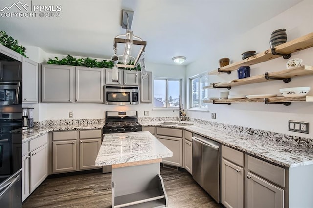 kitchen with appliances with stainless steel finishes, a center island, light stone countertops, gray cabinets, and a sink