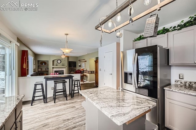 kitchen with a tiled fireplace, a kitchen island, hanging light fixtures, light wood-type flooring, and smart refrigerator