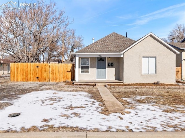 bungalow-style house with a shingled roof, fence, and stucco siding