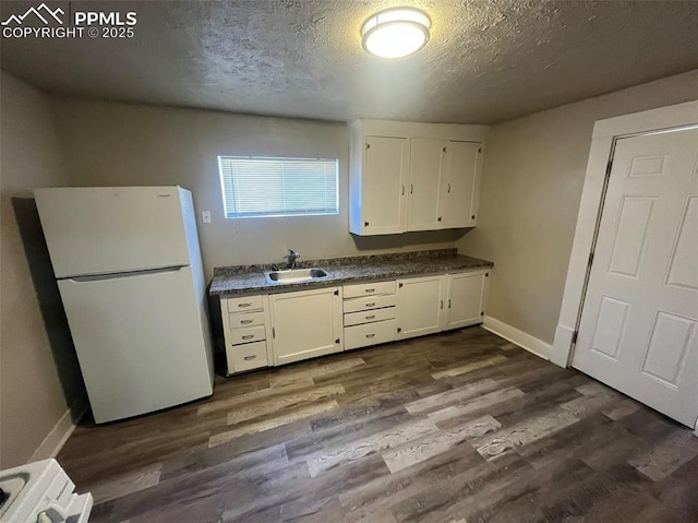 kitchen featuring dark countertops, a sink, freestanding refrigerator, and white cabinetry