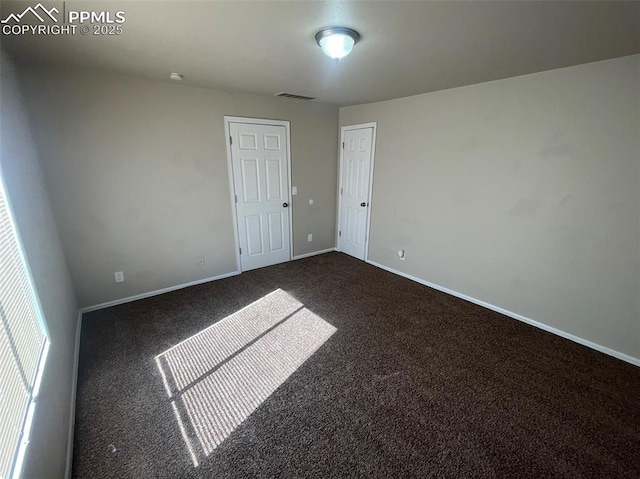 spare room with dark colored carpet, visible vents, and baseboards