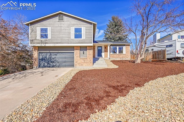 tri-level home with a garage, concrete driveway, brick siding, and fence