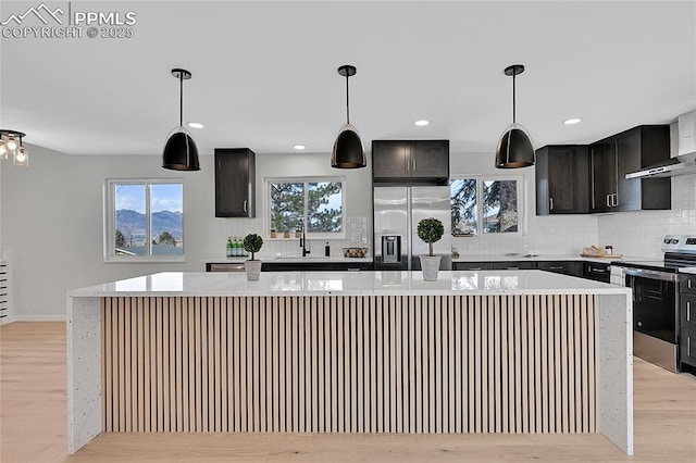 kitchen featuring hanging light fixtures, appliances with stainless steel finishes, a kitchen island, and light wood-style flooring