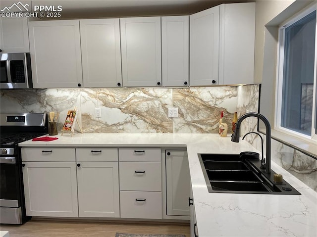 kitchen featuring white cabinetry, stainless steel appliances, light stone countertops, sink, and backsplash