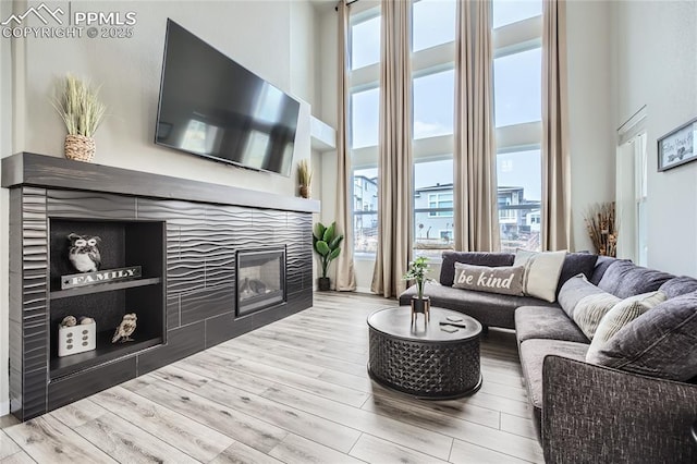 living room with a wealth of natural light, a tiled fireplace, light hardwood / wood-style flooring, and a towering ceiling