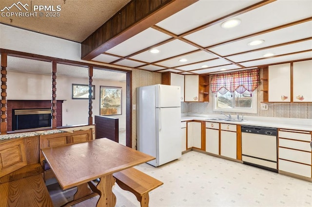 kitchen with white appliances, a sink, light countertops, a brick fireplace, and light floors