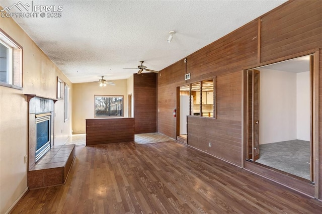 unfurnished living room featuring vaulted ceiling, wood walls, wood finished floors, and a textured ceiling