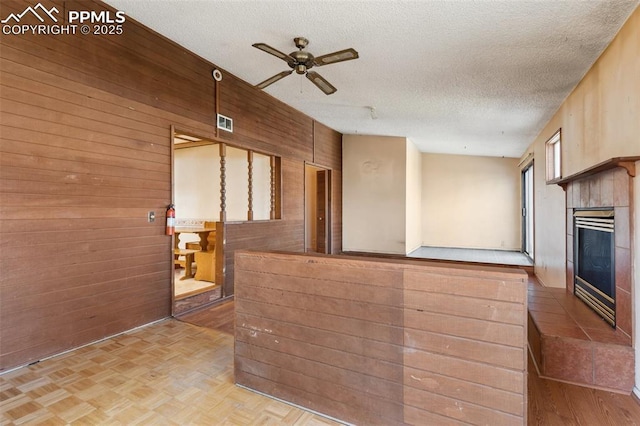 kitchen with a ceiling fan, a fireplace, wooden walls, and a textured ceiling