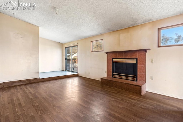 unfurnished living room with a textured ceiling, baseboards, a tiled fireplace, and wood finished floors