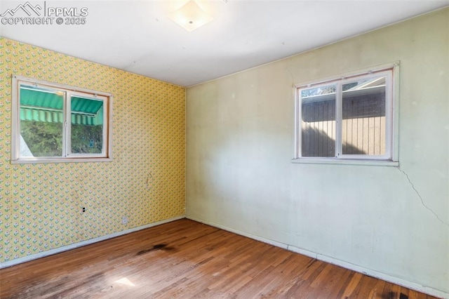 spare room with wallpapered walls, plenty of natural light, baseboards, and wood finished floors