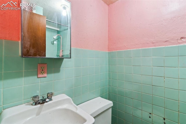 bathroom featuring toilet, tile walls, a sink, and a textured wall