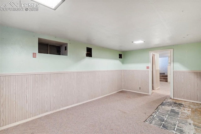 carpeted empty room with a wainscoted wall, wooden walls, and stairs