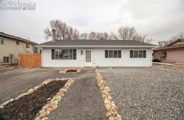 single story home featuring driveway, a shingled roof, and fence