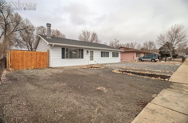 ranch-style home with driveway, a chimney, and fence