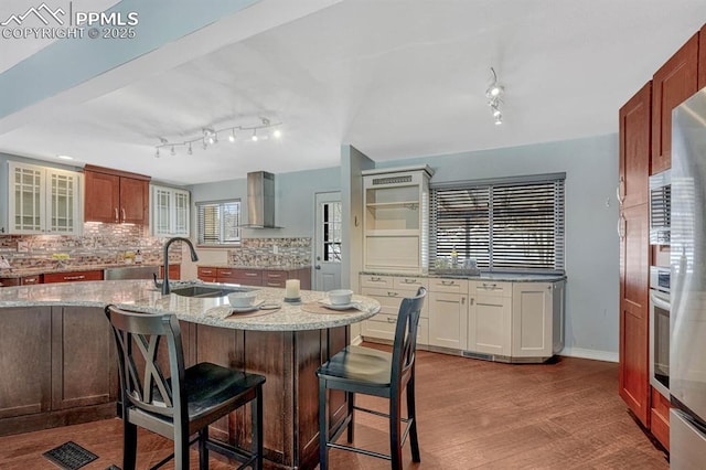 kitchen with decorative backsplash, a breakfast bar area, light wood-type flooring, wall chimney range hood, and a sink