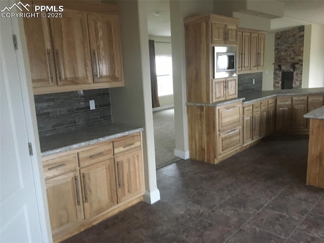 kitchen featuring a fireplace, tasteful backsplash, light countertops, stainless steel microwave, and light brown cabinets