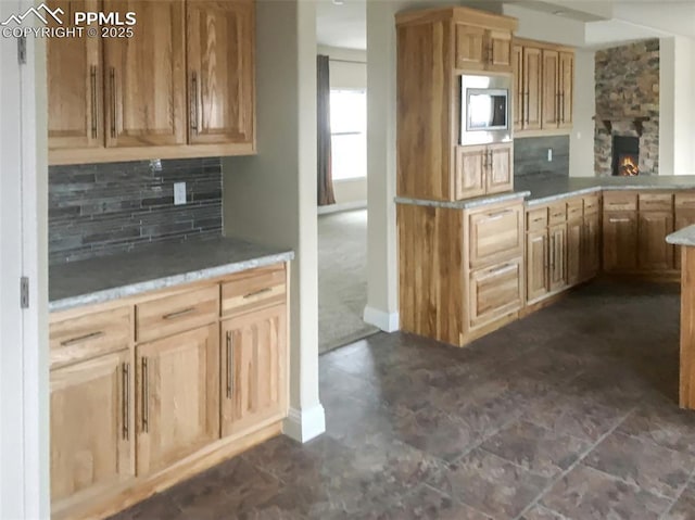 kitchen with tasteful backsplash, light countertops, stainless steel microwave, and a stone fireplace