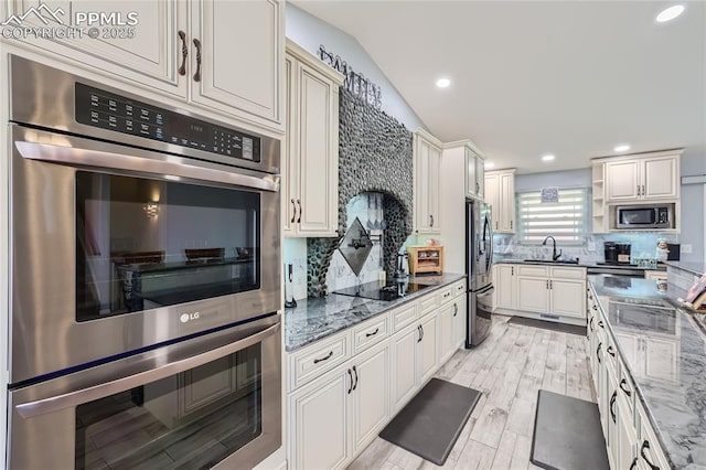 kitchen featuring dark stone counters, stainless steel appliances, backsplash, and a sink