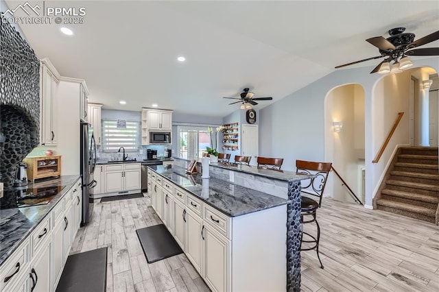 kitchen with appliances with stainless steel finishes, a breakfast bar area, dark stone countertops, and white cabinets