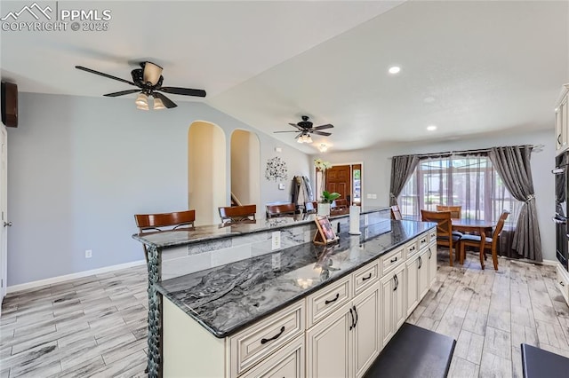 kitchen featuring arched walkways, light wood-style flooring, a ceiling fan, white cabinets, and dark stone counters