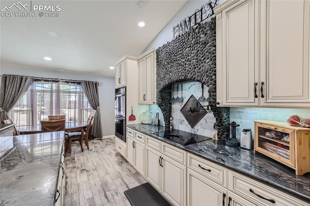 kitchen with black electric stovetop, decorative backsplash, cream cabinets, stainless steel double oven, and dark stone counters