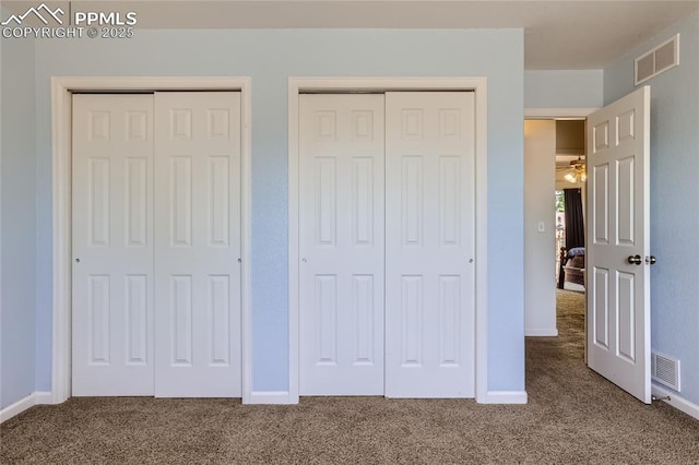 unfurnished bedroom featuring two closets, baseboards, visible vents, and carpet flooring