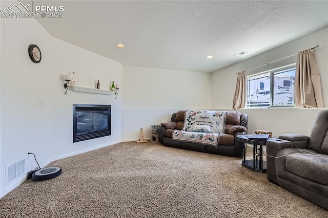 living room with baseboards, visible vents, a glass covered fireplace, a textured ceiling, and carpet floors