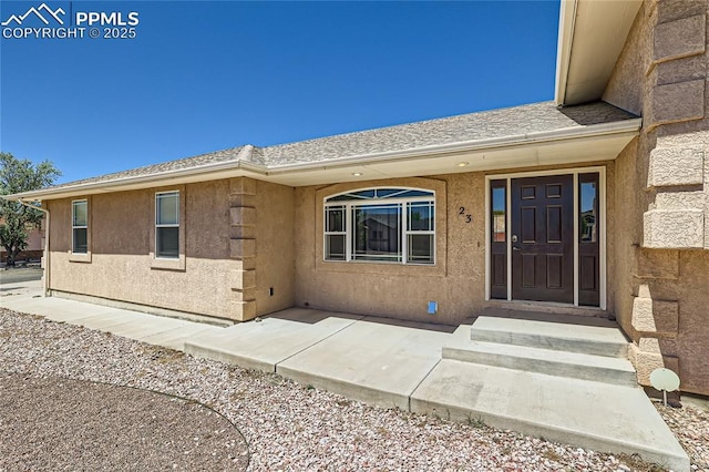 entrance to property with roof with shingles and stucco siding