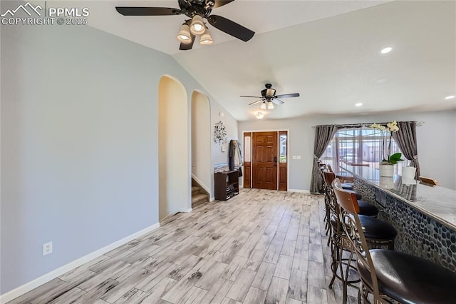 interior space featuring light wood finished floors, baseboards, arched walkways, lofted ceiling, and stairway