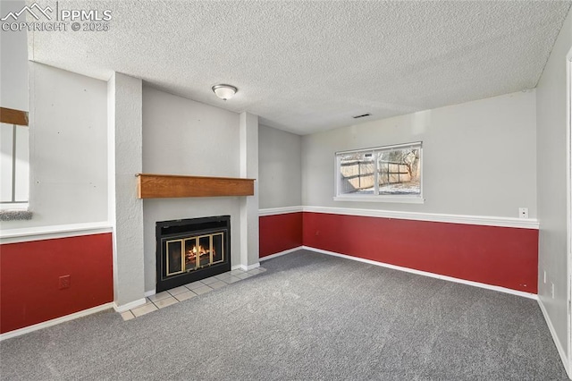 unfurnished living room featuring a fireplace with flush hearth, baseboards, a textured ceiling, and light colored carpet