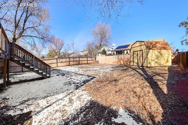 yard covered in snow with a storage shed, a fenced backyard, stairs, and an outbuilding