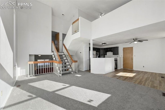 unfurnished living room featuring dark wood-style flooring, a towering ceiling, a ceiling fan, stairs, and dark carpet