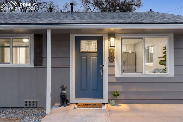 view of exterior entry with a shingled roof and visible vents