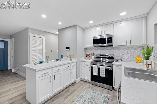 kitchen with a peninsula, a sink, white cabinets, light countertops, and appliances with stainless steel finishes